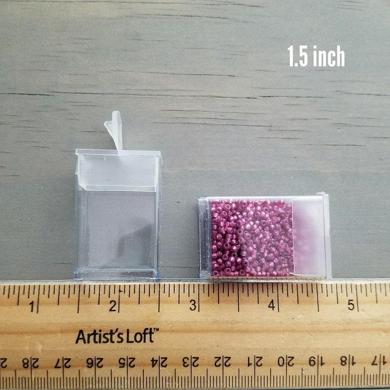 May include: Two clear plastic containers with lids, one filled with pink seed beads. The containers are 1.5 inches tall and are measured against a ruler.