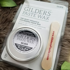May include: A silver-colored tin of Gilders Paste Wax, a colorizing wax for wood finishing. The tin is labeled with the product name, color, and size: 1 oz (30 ml). The packaging also includes a wooden applicator.
