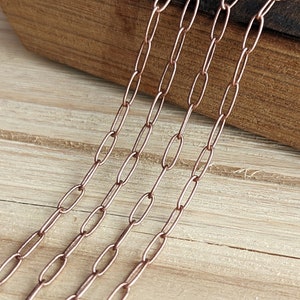 May include: Close-up of a copper chain with oval links. The chain is lying on a wooden surface.