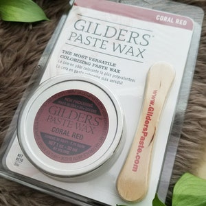 Op de afbeelding: Een klein potje met koraalrode GILDERS Paste Wax, een veelzijdige kleurwas voor houtbewerking. Het potje is gelabeld met de merknaam, productnaam, kleur en dekking. Het bevat een houten applicator stick met de website van het merk erop gedrukt.