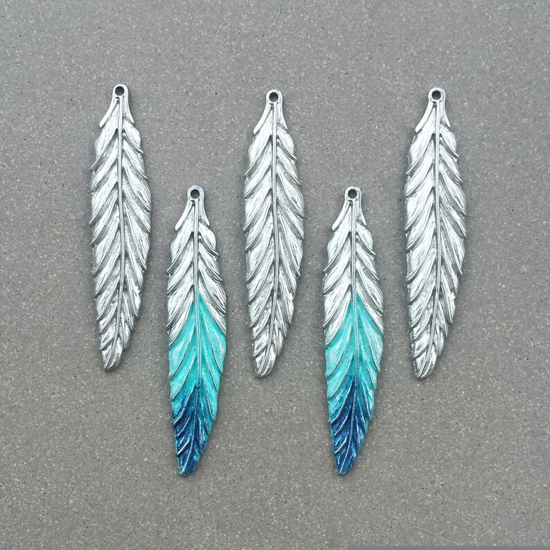May include: Five silver feather charms with a blue and turquoise ombre paint finish. The charms have a hole at the top for attaching to jewelry or other crafts.