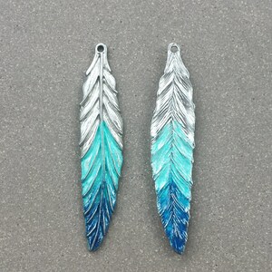 May include: Two silver-toned metal feather charms with a blue and turquoise ombre paint finish.