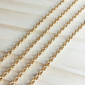 May include: Four strands of gold chain link, laid out in parallel lines on a light wood surface.