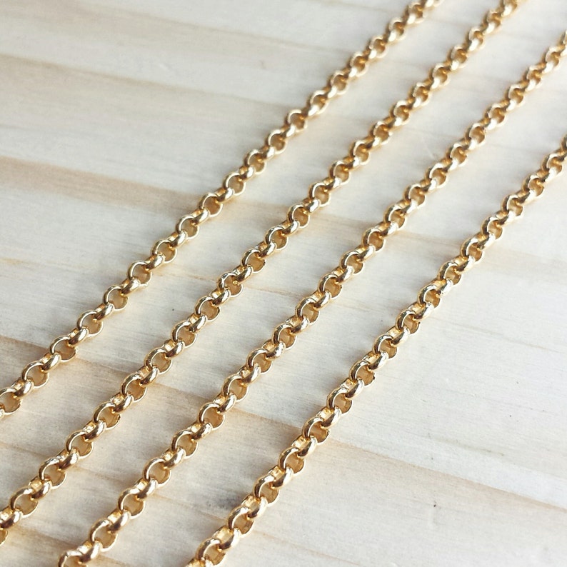 May include: Four strands of gold chain link, laid out in parallel lines on a light wood surface.