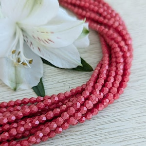 Peut inclure: Un brin de perles de verre facettées rouges. Les perles sont petites et ont une finition brillante. Les perles sont disposées en cercle.