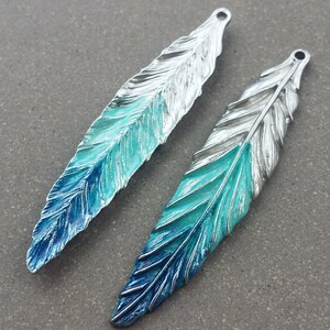 May include: Two silver-toned feather charms with a blue and turquoise gradient enamel finish. The feathers have a detailed design and are perfect for jewelry making.
