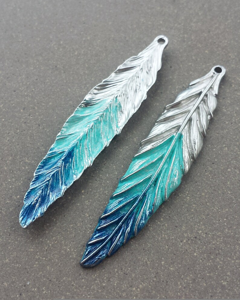 May include: Two silver-toned feather charms with a blue and turquoise gradient enamel finish. The feathers have a detailed design and are perfect for jewelry making.
