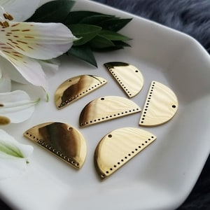 Pode incluir: Seis componentes de joalharia em metal dourado em forma de semicírculo com um acabamento polido. Cada peça tem uma fila de pequenos orifícios ao longo da borda curva e um único orifício na parte superior. Os componentes estão dispostos numa superfície branca com uma flor e vegetação.