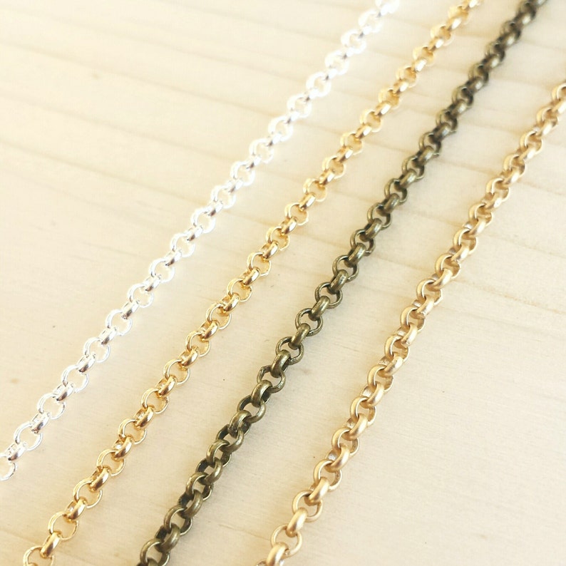 May include: Four chains of different colors: silver, gold, bronze, and brass. The chains are laid out in a row on a light wood surface.