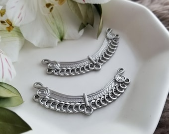 May include: Two silver metal jewellery connectors with a decorative design. Each connector has a curved shape with a row of small circles and a larger circle at the top.