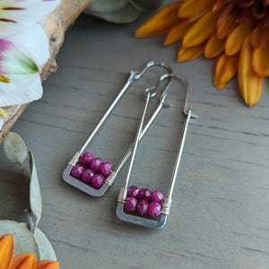 May include: A pair of silver earrings with a rectangular design. Each earring features a cluster of five pink gemstone beads.
