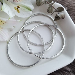 May include: Four silver bangles with a hammered texture. The bangles are stacked on top of each other.