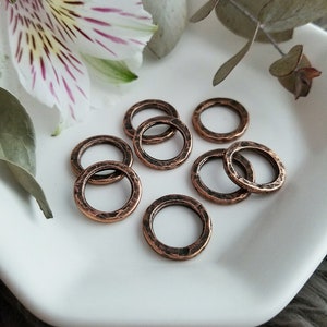 May include: A set of eight copper-colored jump rings with a hammered texture. The rings are arranged on a white surface.