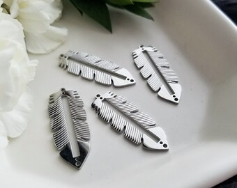 May include: Four silver metal feather charms with a textured design. The charms are on a white surface.