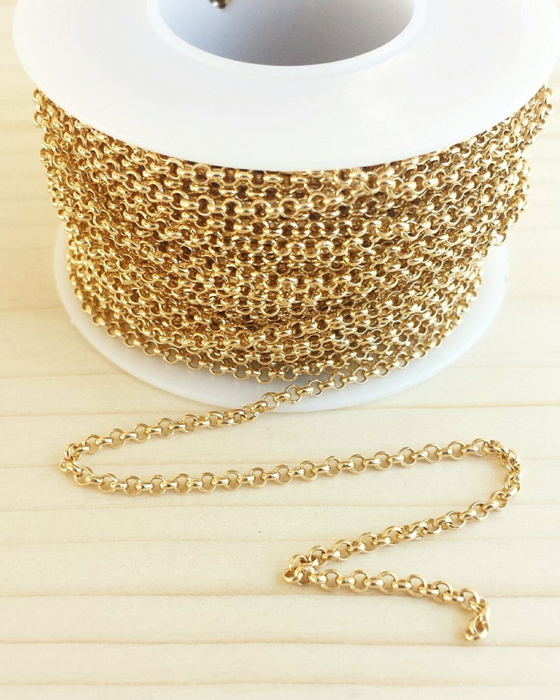 May include: A spool of gold-colored chain, with a small section of the chain uncoiled and lying on a wooden surface.