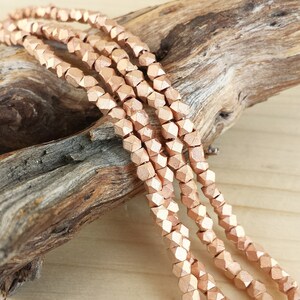 May include: A strand of rose gold faceted beads. The beads are small and have a geometric shape. The beads are strung on a wire and are ready to be used in jewelry making.