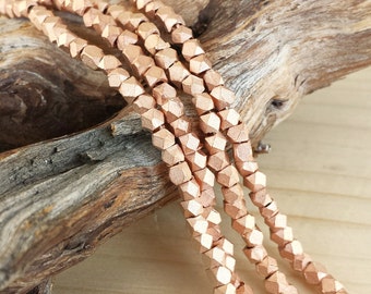 Op de afbeelding: Een streng roze gouden facetgeslepen kralen. De kralen zijn klein en hebben een geometrische vorm. De kralen zijn geregen op een draad en zijn klaar om te worden gebruikt voor het maken van sieraden.