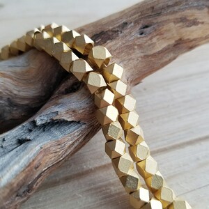 以下が含まれることがあります： 金色のファセットカットビーズのストランド。ビーズは一列に並べられ、互いに積み重ねられています。ビーズは木でできており、光沢のある仕上げになっています。