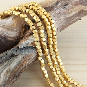 May include: Close-up of several strands of gold-colored, faceted beads. The beads have a matte finish and are strung together. The background features a piece of weathered wood and a light-colored wooden surface.