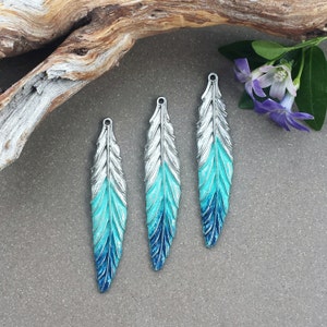 May include: Three silver-toned metal feather charms with a blue and turquoise ombre paint finish.
