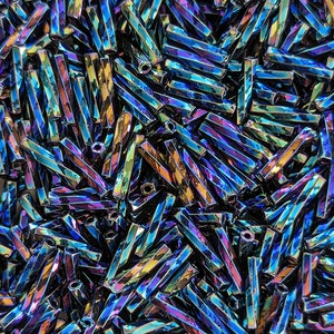 May include: A close-up shot of a pile of iridescent, rectangular beads. The beads have a faceted surface that reflects a spectrum of colors, including blues, greens, and yellows. Each bead is approximately 0.25 inches long. The beads are scattered.