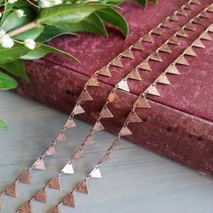 May include: Three strands of copper chain with triangle-shaped charms. The chain is lying on a burgundy book.