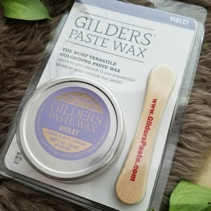 Puede incluir: Una pequeña lata de cera para colorear GILDERS PASTE WAX de color violeta, con un aplicador de madera. La etiqueta dice "THE MOST VERSATILE COLORIZING PASTE WAX" y "COVERS 30 SQ/FT - 2.78 SQ/M NET 1 oz - 30 ml BY VOLUME".