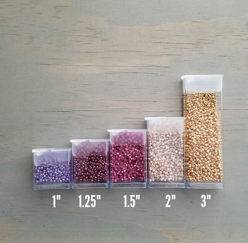 May include: Five clear plastic containers filled with different colored seed beads. The containers are lined up from smallest to largest, with the smallest container being 1 inch wide and the largest container being 3 inches wide. The beads are purple, burgundy, dark red, white, and gold.