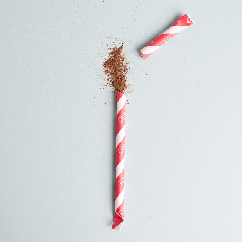May include: A red and white striped paper straw with a red and white striped paper straw on a light blue background. The straw is broken in half and the top half is laying on the bottom half. There is a pile of brown powder on the bottom half of the straw.