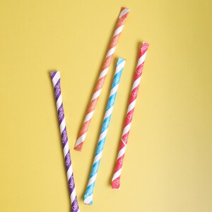 May include: Four striped paper straws in different colors: purple, orange, blue, and red. The straws are on a yellow background.