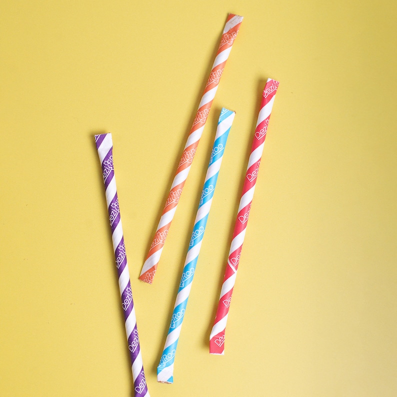 May include: Four striped paper straws in different colors: purple, orange, blue, and red. The straws are on a yellow background.