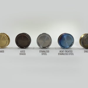 May include: Five round metal discs in different finishes: brass, aged brass, stainless steel, heat-treated stainless steel, and engraved brass. The engraved disc has the letters "AJM" on it.