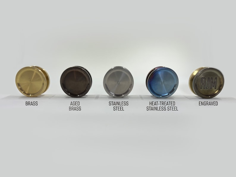 May include: Five round metal discs in different finishes: brass, aged brass, stainless steel, heat-treated stainless steel, and engraved brass. The engraved disc has the letters "AJM" on it.