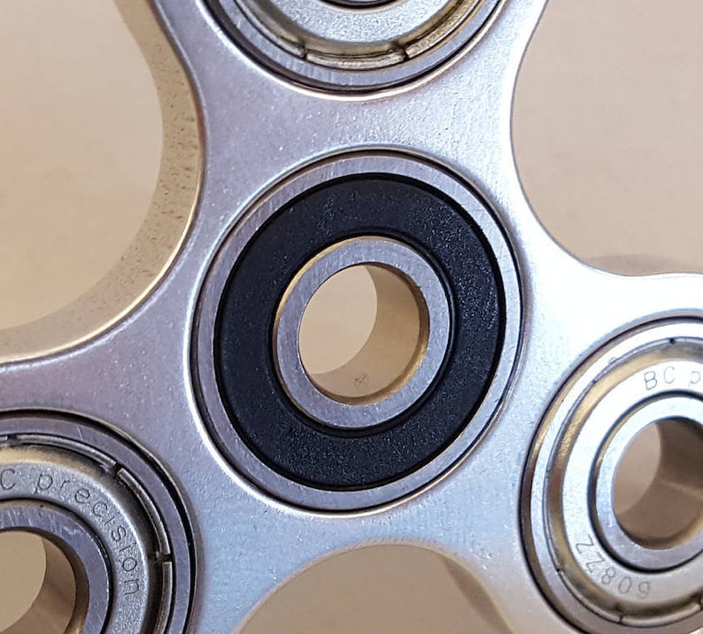 May include: A silver fidget spinner with five arms and five bearings. The bearings are black and silver and have a smooth, polished finish.