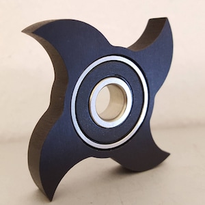 Puede incluir: Un spinner de dedos negro con forma de estrella de cinco puntas y un rodamiento plateado en el centro.