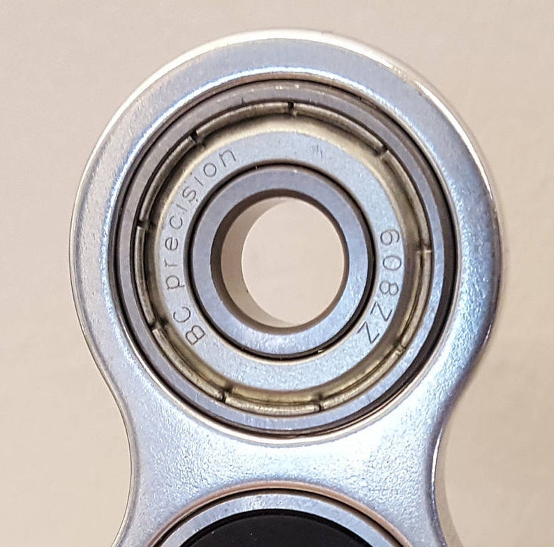 May include: Close-up of a silver fidget spinner with a bearing that reads "BC Precision ZZ 809".