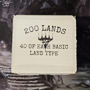 May include: A white rectangular box with the text "200 LANDS" and "40 OF EACH BASIC LAND TYPE" in black. The box features a black and white graphic. The background is a dark, patterned surface.