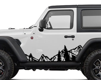 May include: A white Jeep Wrangler with black accents and a black hardtop. The side of the vehicle features a black mountain and tree decal. The tires are black with silver rims. A spare tire is mounted on the back.