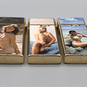 May include: Three rectangular gold-tone metal lighters with the text PENGUIN SHARP engraved on the bottom. Each lighter features a different photographic print of a person on the front surface, showcasing varied outdoor and indoor settings.