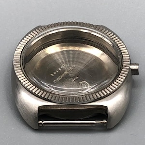 May include: A stainless steel watch case with a fluted bezel and a clear crystal. The case has a brushed finish and a crown on the side. The watch case is empty, with the back visible.