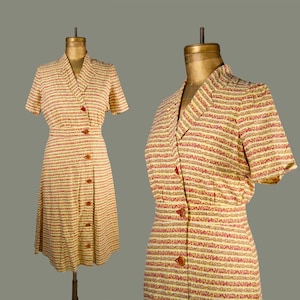 May include: A short-sleeved dress featuring a cream base with horizontal stripes in red and brown. The dress has a notched collar, a fitted waist, and a front button closure with brown buttons. The fabric displays a repeating textured pattern.
