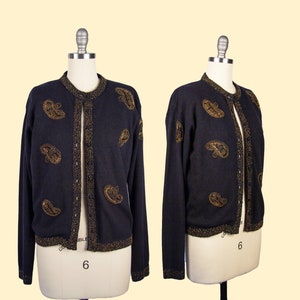 Peut inclure: Un cardigan noir avec des broderies dorées en forme de paisley. Le cardigan a une fermeture boutonnée et des manches longues.