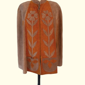 May include: A suede cape in shades of brown and orange featuring a front zipper closure and a high collar. The garment is decorated with large, appliqu&eacute;d floral motifs in brown suede on the orange front panels and two lower patch pockets.