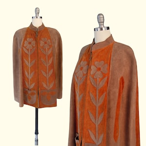 May include: A suede cape in shades of brown and orange featuring a front zipper closure and a high collar. The garment is decorated with large, appliqu&eacute;d floral motifs in a lighter brown tone, extending from the hem to the chest area.