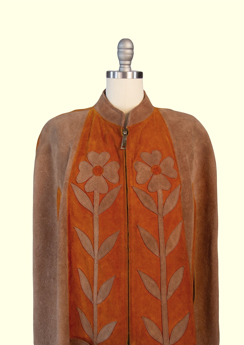 May include: A brown and orange suede jacket featuring a stand-up collar and a full-length front zipper. The front panels are decorated with large, appliqu&eacute;d brown flower motifs with long stems and leaves centered on the vibrant orange suede sections.