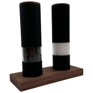 Peut inclure: Deux moulins à poivre et à sel électriques noirs avec des contenants en verre transparent remplis de grains de poivre et de sel. Les moulins sont sur une base en bois.