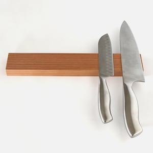 May include: A wooden magnetic knife holder with two silver knives attached. The holder is made of light brown wood and has a smooth surface.