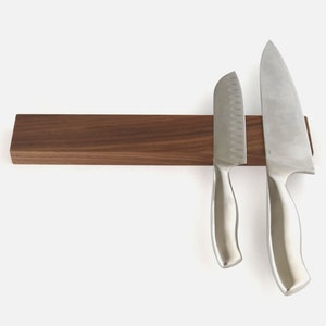 May include: A walnut wood magnetic knife holder with two silver knives attached to it.