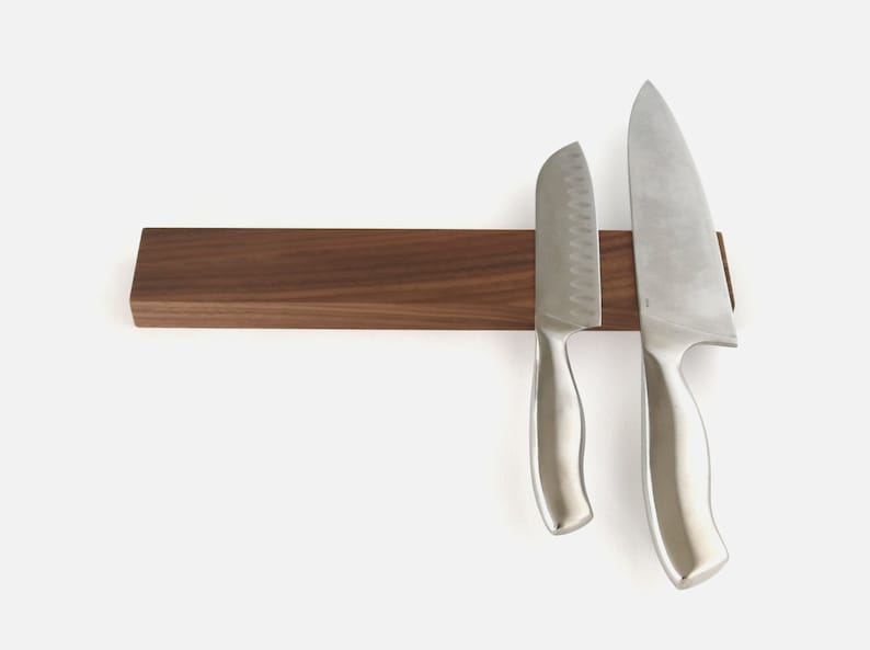 May include: A walnut wood magnetic knife holder with two silver knives attached to it.