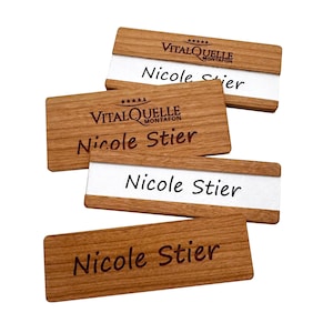 Könnte beinhalten: Eine Sammlung von Namensschildern aus Holz mit dem Namen "Nicole Stier". Die Namensschilder haben eine helle Holzmaserung mit einem weißen Mittelteil. Einige Schilder enthalten auch den Text "VITALQUELLE MONTAFON".
